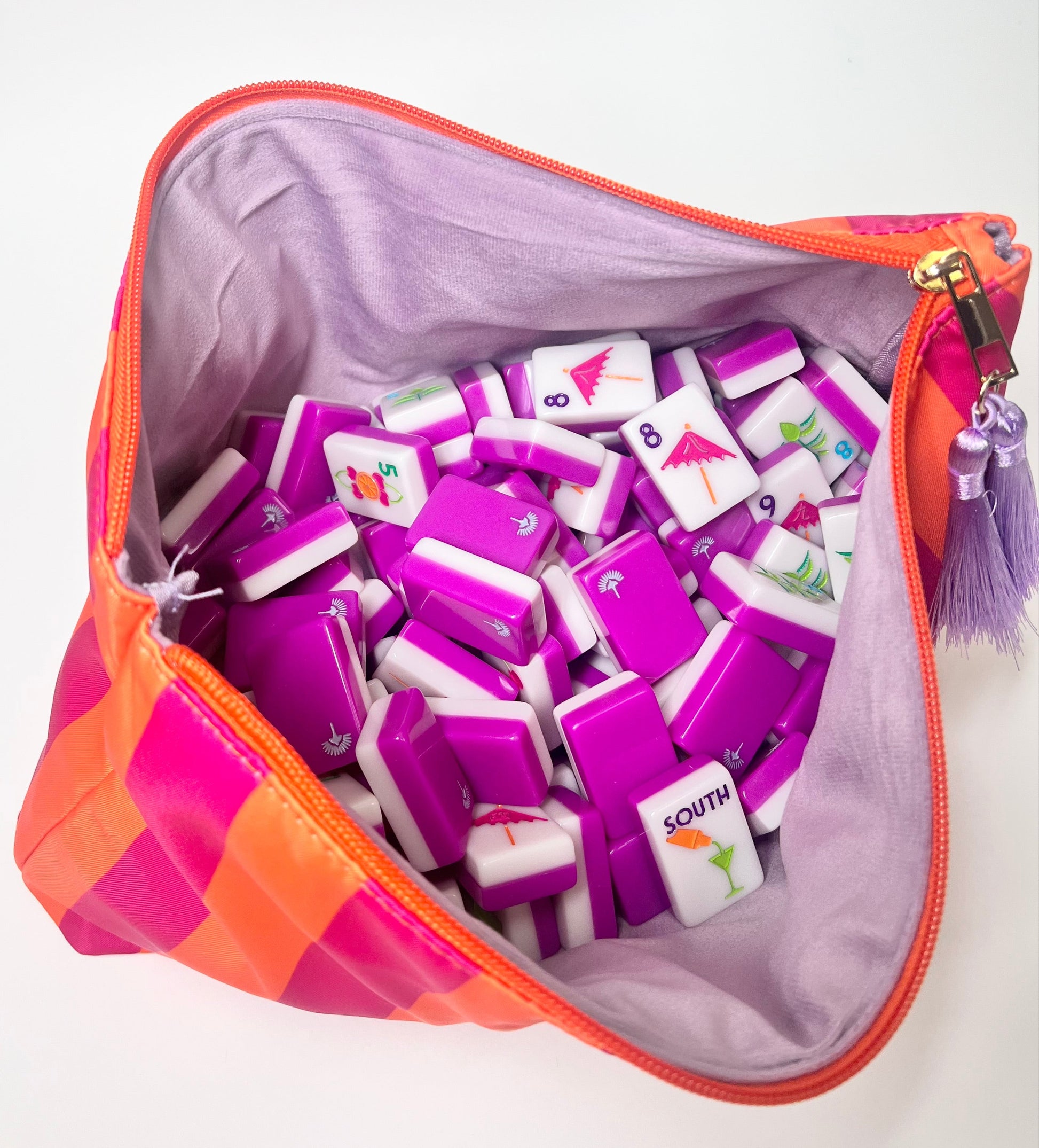 Pink and orange bag with light purple velvet liner filled with purple and white game pieces on a white background