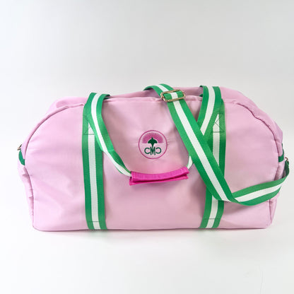 Pink duffel bag with green straps on a white background