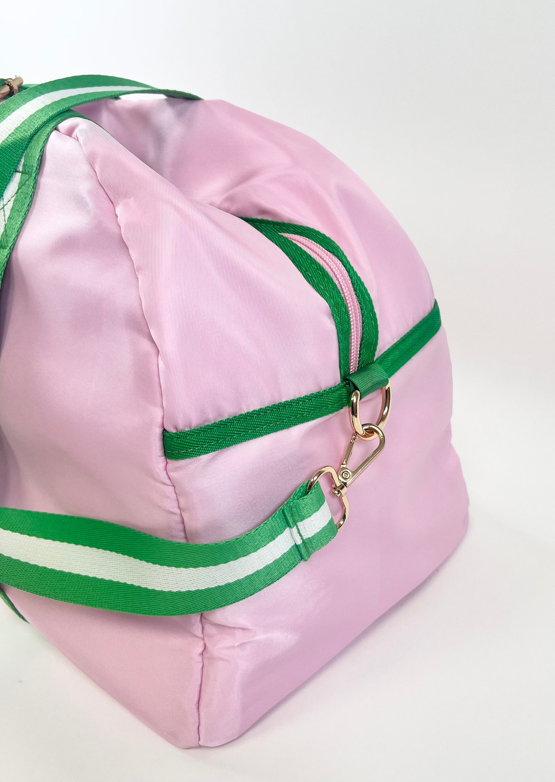 Pink duffel with green and white straps with cross body strap on a white background